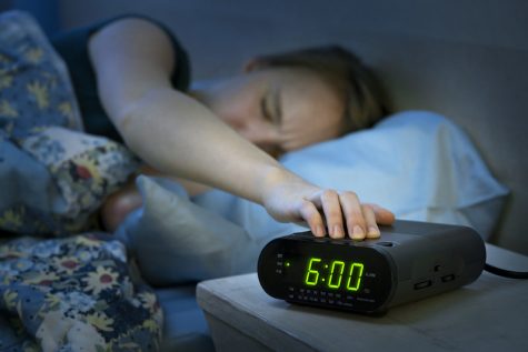 Young woman pressing snooze button on early morning digital alarm clock radio.