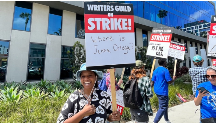 People+walking+around+holding+up+their+Writers+Guild+on+Strike%21+signs.