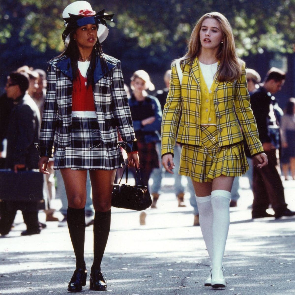 Cher Horowitz (Alicia Silverstone) wearing a yellow and plaid matching set as she walks with Dionne Davenport (Stacey Dash) who is wearing a dark blue and plaid matching set.