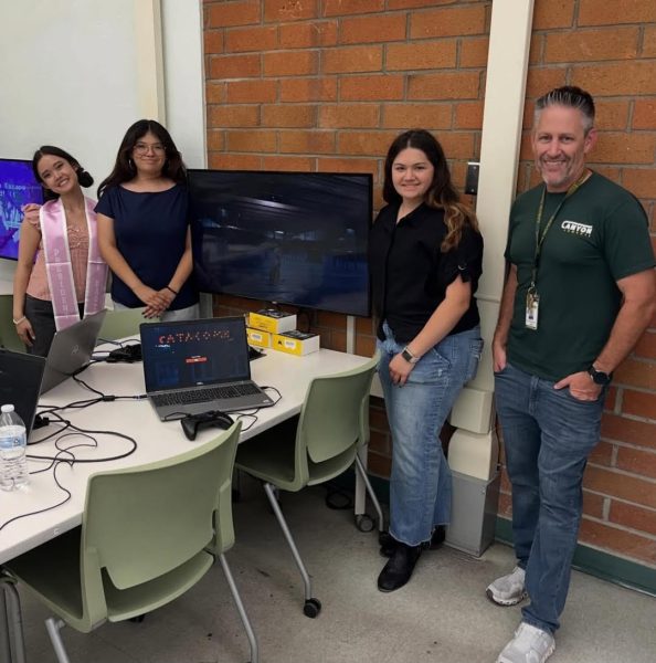 Three students posing with Mr. Underwood in front of their game on Demo Day!
